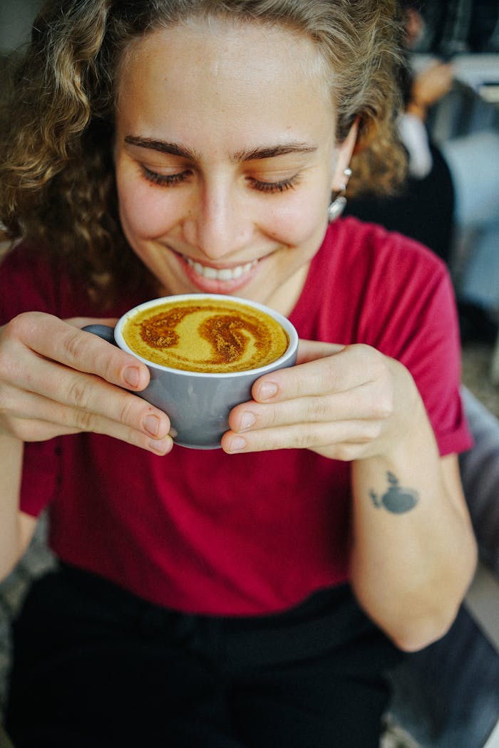 Smiling woman holding a turmeric latte indoors, wearing a red t-shirt. Perfect for lifestyle stock photos.